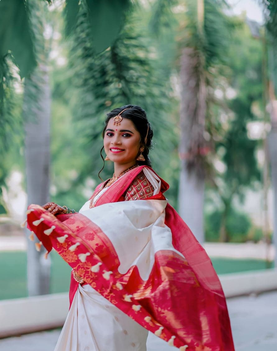 Bride twirling the pallu of her cream and red silk saree, smiling beneath a canopy of palm trees